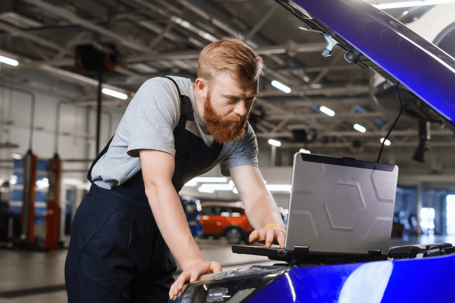 Professional automotive electrician diagnoses car errors using laptop against background service station 1